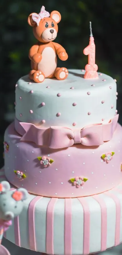 Pink birthday cake with bear topper and candle.