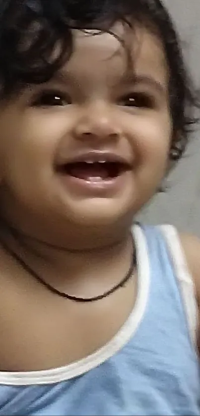 Adorable baby in blue tank top smiling joyfully.