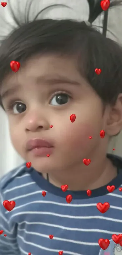 Cute toddler with playful hair in a blue striped shirt on white wall.