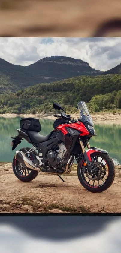 Red adventure bike by a tranquil lake with mountains backdrop.