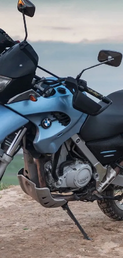 Sky-blue motorcycle on a hilltop overlooking a city at dusk.