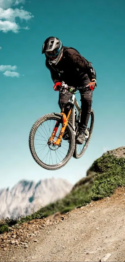 Cyclist mid-air on mountain terrain under a clear blue sky.