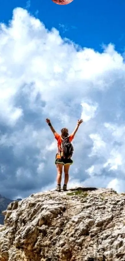 Hiker on rocky mountain under a cloudy sky, arms raised triumphantly.