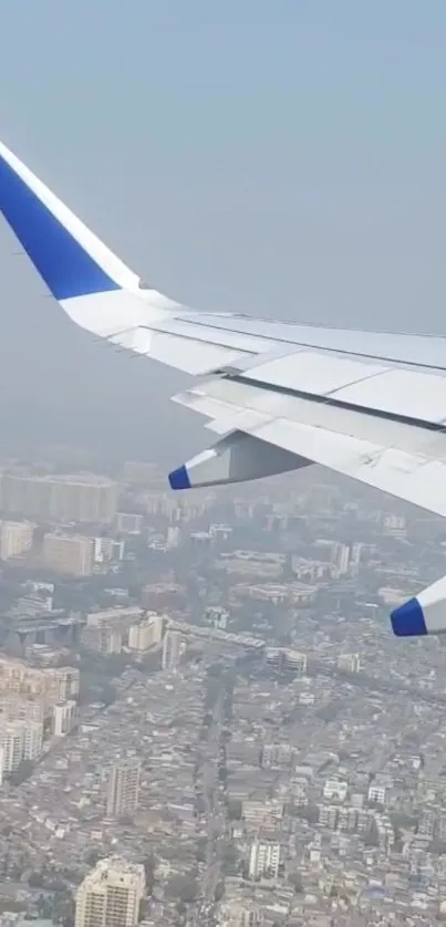 Airplane wing over city with blue sky.