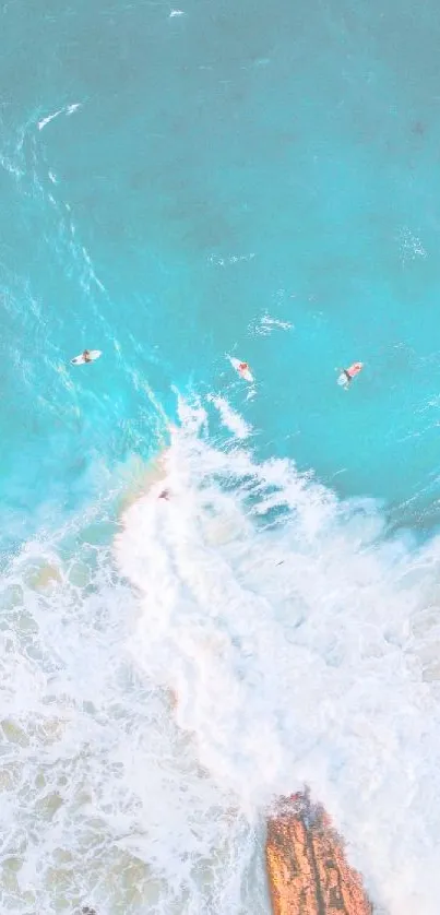 Aerial view of surfers in turquoise ocean waves and rocky beach.