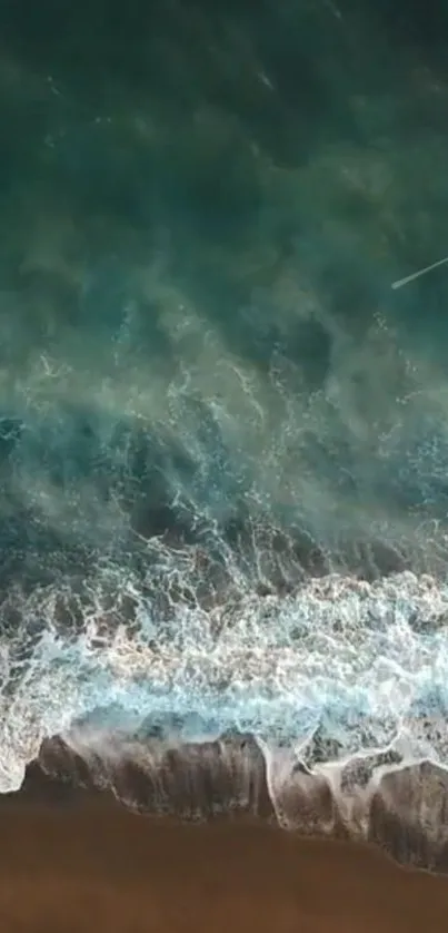 Aerial view of ocean waves crashing on a serene beach with teal and blue hues.