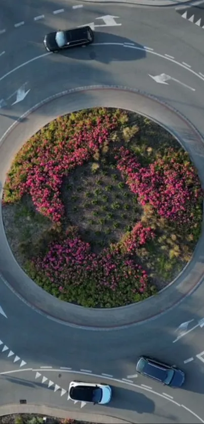 Aerial view of a roundabout with cars and pink flowers.