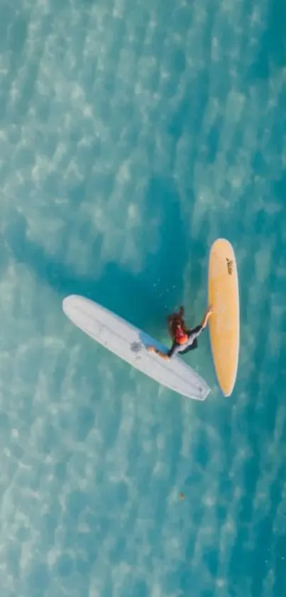 Aerial view of a surfer navigating vibrant aquamarine waters with two surfboards.