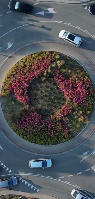 Aerial view of a lively city roundabout with pink flowers and traffic.