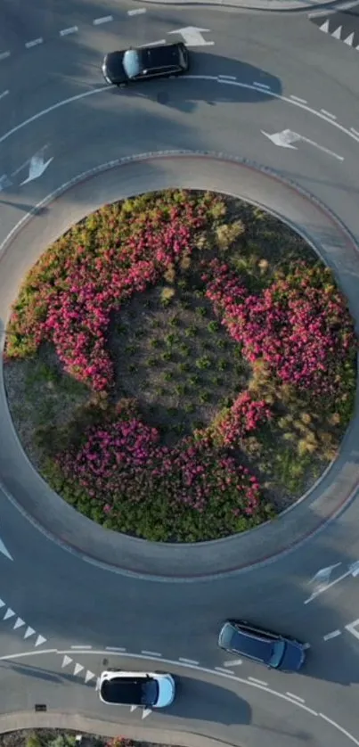 Aerial view of a roundabout with pink flowers and cars.