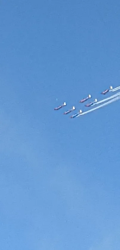 Aerobatic planes flying in formation across a bright blue sky.