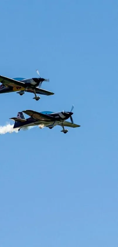 Two airplanes performing stunts in a clear blue sky with trails of smoke.