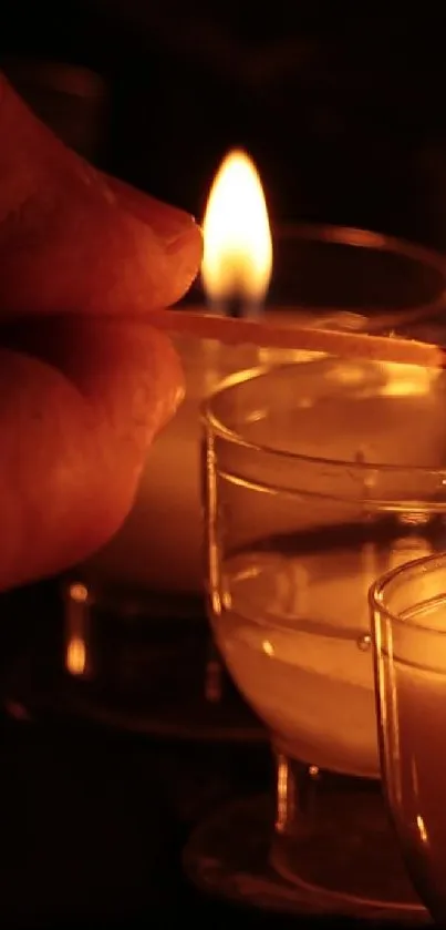 Hand lighting candles with warm, glowing flames in the dark.