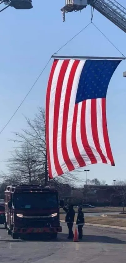 American flag hoisted by two ladder trucks in an outdoor urban area.