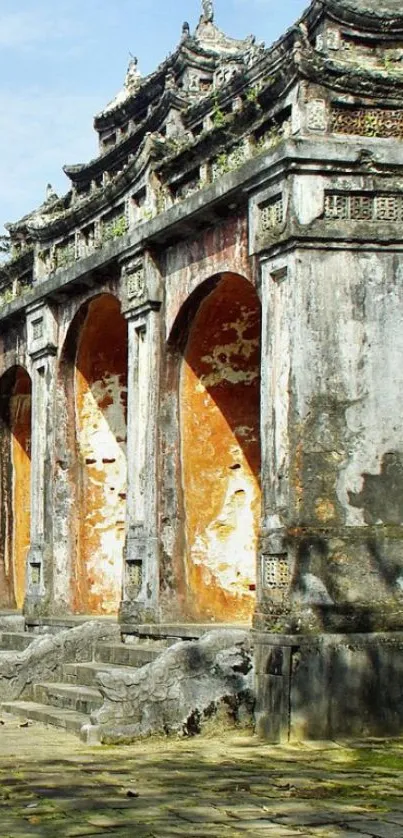 Ancient temple facade with arches and textured stone walls under a blue sky.