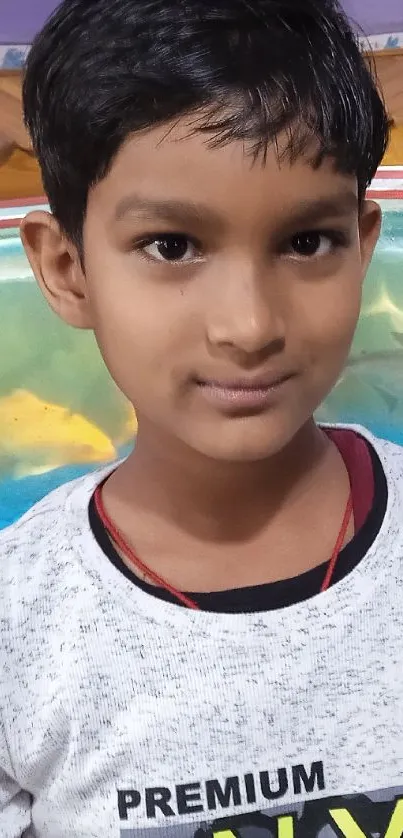 Boy poses in front of colorful fish aquarium, vibrant blue backdrop.