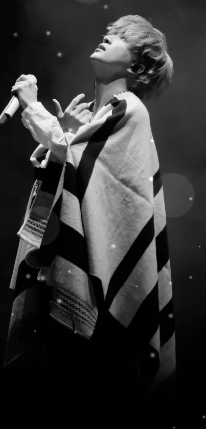 Monochrome image of a singer in a cloak with a microphone on stage.