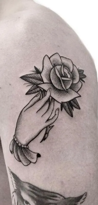 Black and white tattoo of hand holding rose on arm.