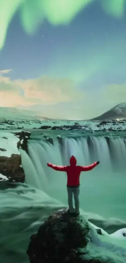 Person stands before a waterfall under a vibrant green aurora.