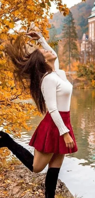 Woman in red skirt near autumn lake with castle in background.