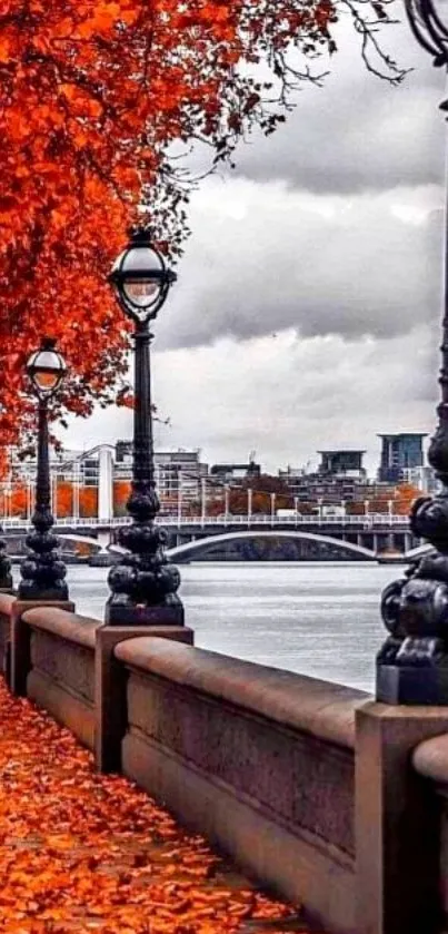 Autumn leaves line a riverside walkway with street lamps.