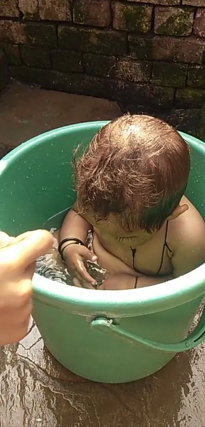 Baby in a teal green bucket enjoying a bath outdoors.