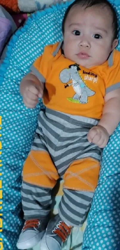 Baby lying in colorful bedding with orange and blue accents.