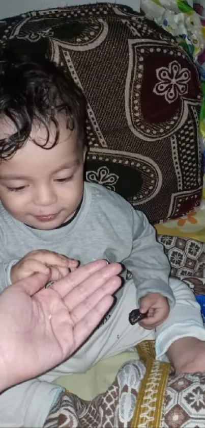 Smiling baby playing with a coin on a patterned sofa.