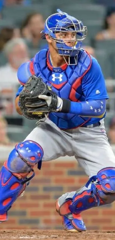 Baseball catcher in blue gear crouching on the field during a game.