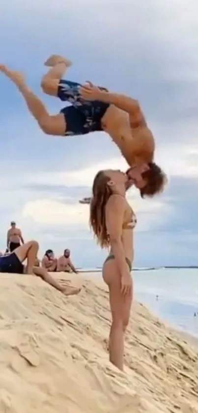 Couple kissing with acrobatic flip on sandy beach.