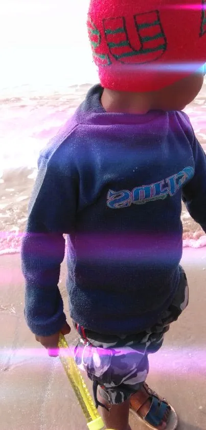 Child playing by the sea wearing a red hat.