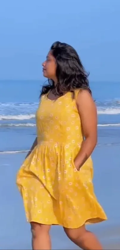 Woman in yellow dress walking along a serene beach with blue sky.