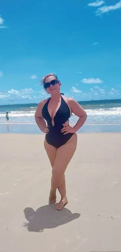 Person enjoying a sunny day on a sandy beach with blue sky and ocean.