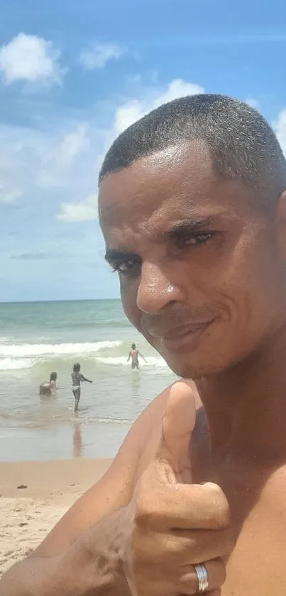 Man giving a thumbs up at the beach against a blue sky.