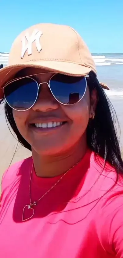 Person in sunglasses and hat smiling at the beach.