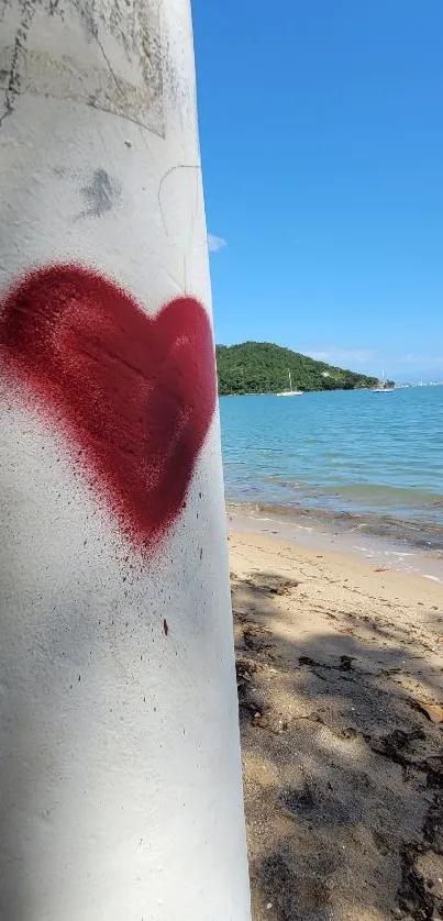 Heart graffiti on a beach with blue sky and distant green hills.