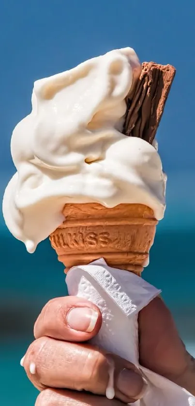 Ice cream cone held against ocean backdrop on sunny beach.