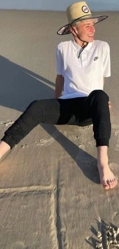 Person relaxing on a sandy beach wearing a sun hat and casual attire.