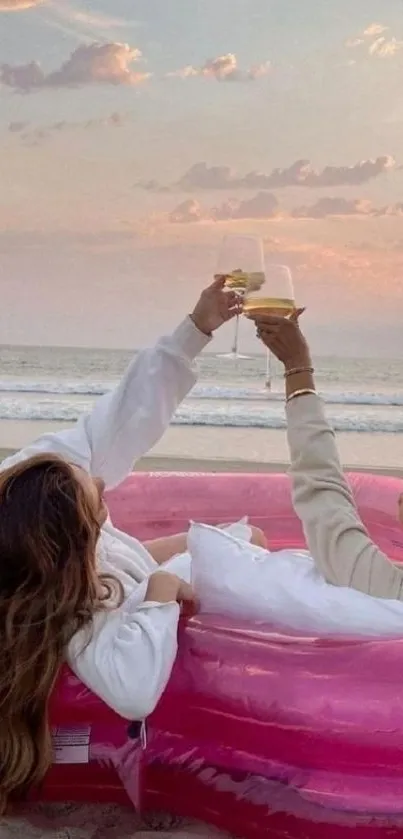 Two people relaxing on a beach in a pink inflatable pool, toasting at sunset.