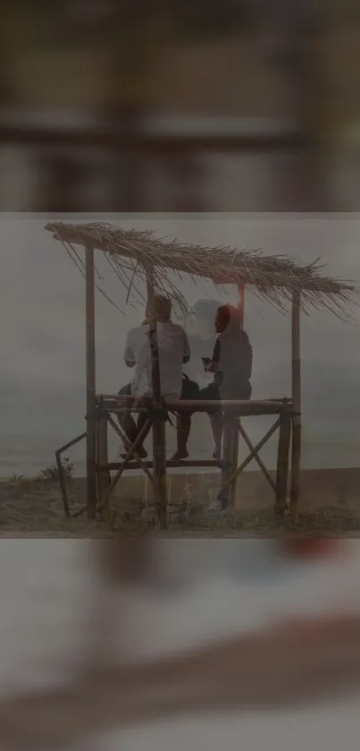 Friends enjoying a serene sunset on a beach under a rustic shelter.