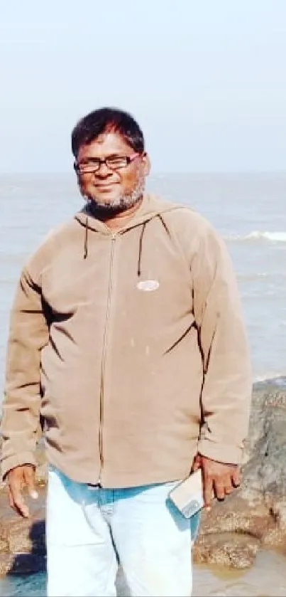 Man in hoodie at the beach, enjoying a serene ocean view background.