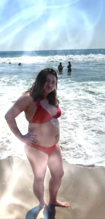 A woman in a red bikini at the beach with ocean waves.