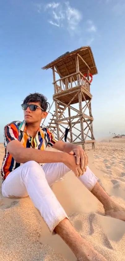 Man in colorful shirt relaxing on sandy beach with lifeguard tower.