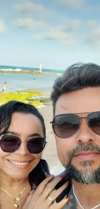 Couple taking a selfie on a sunny beach with ocean background.