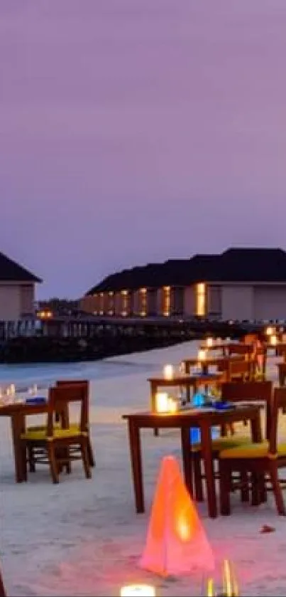 Candlelit tables on beach with purple sky.