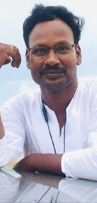 Man in white shirt leaned against a car, posing on a beach with reflection.