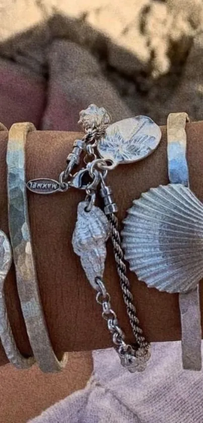 Beachy bracelet with silver seashell charms on a sandy background.