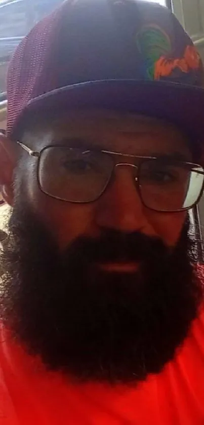 Bearded man in vibrant hat and glasses posing casually.