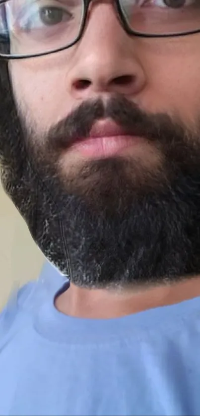 Portrait of a bearded man with glasses wearing a light blue shirt.