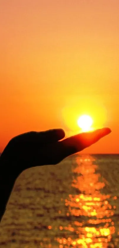 Silhouette of a hand holding the sun during a vibrant ocean sunset.